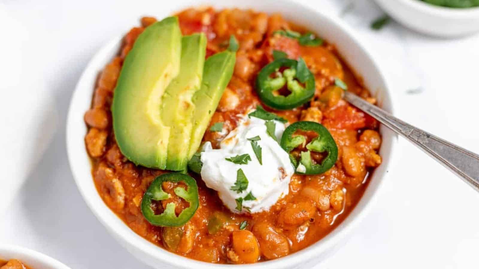 A bowl of chili topped with avocado and peppers.