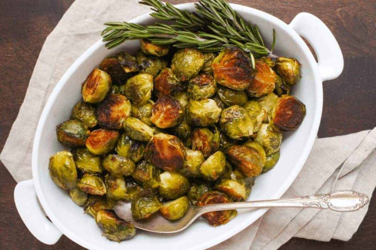 A white serving dish filled with roasted brussels sprouts and fresh rosemary.