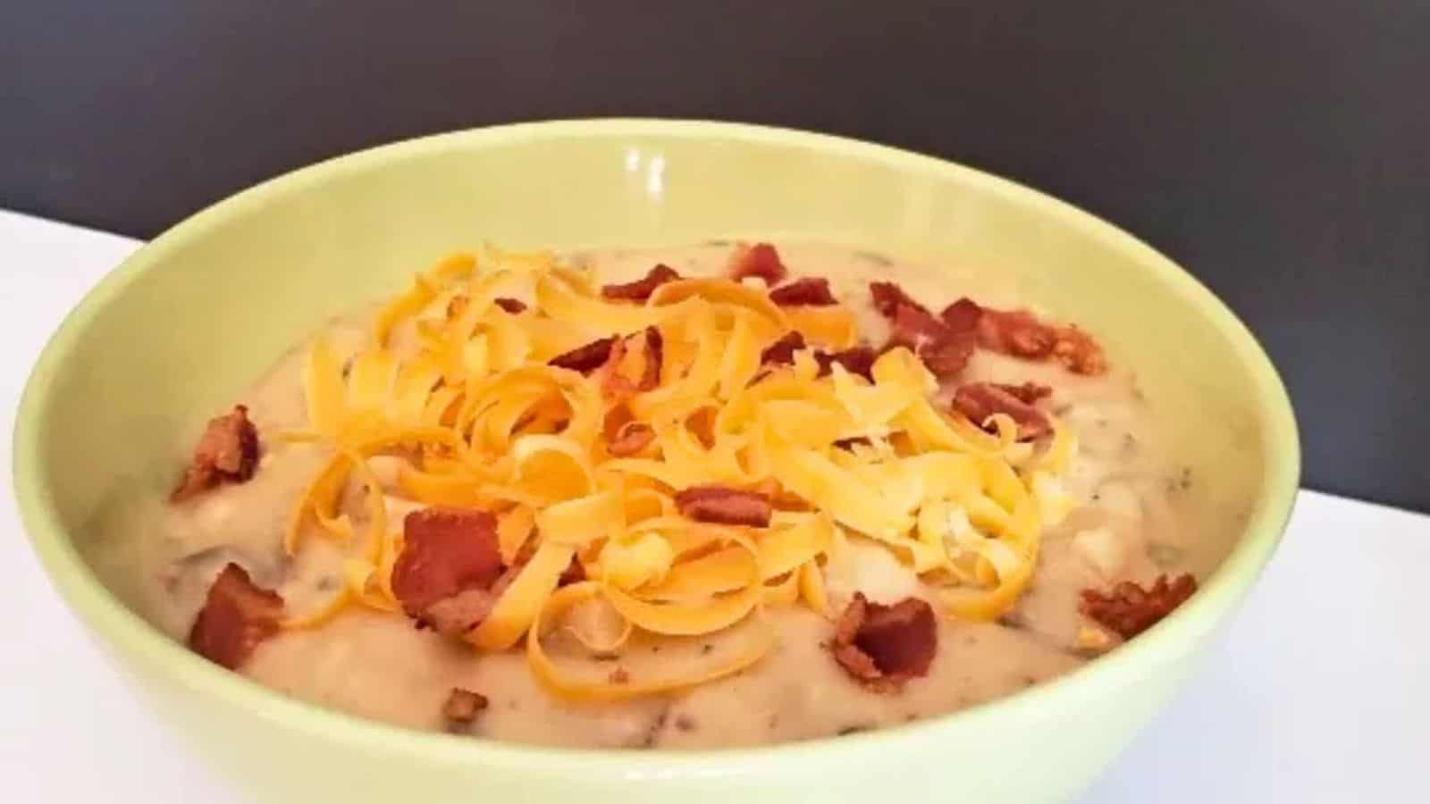 Image shows A bowl of cheesy loaded baked potato soup with bacon and cheese.