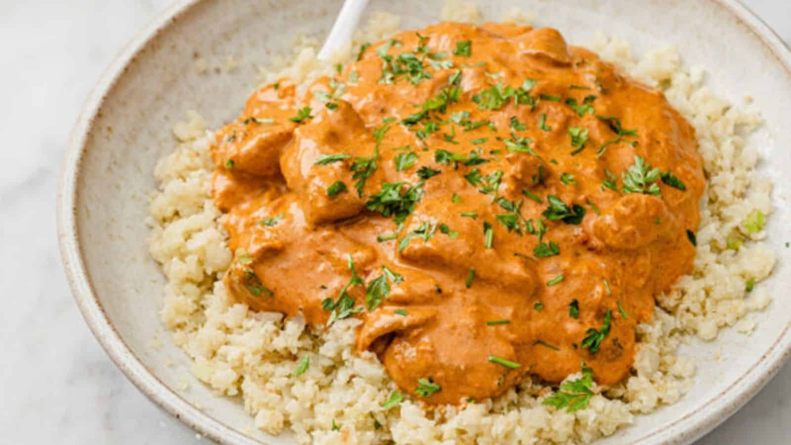 Close-up image of instant pot butter chicken on top of cauliflower rice in a plate.