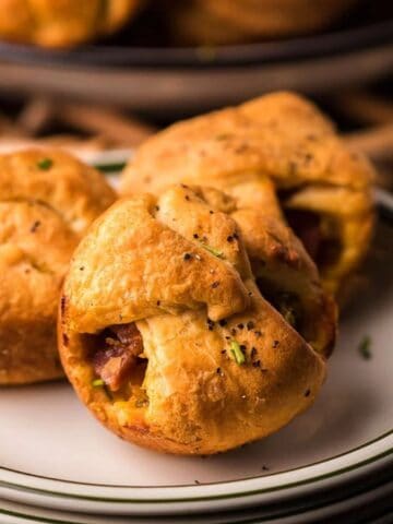 Three Leftover Ham, Broccoli and Cheese Crescent Cups on a stack of plates.