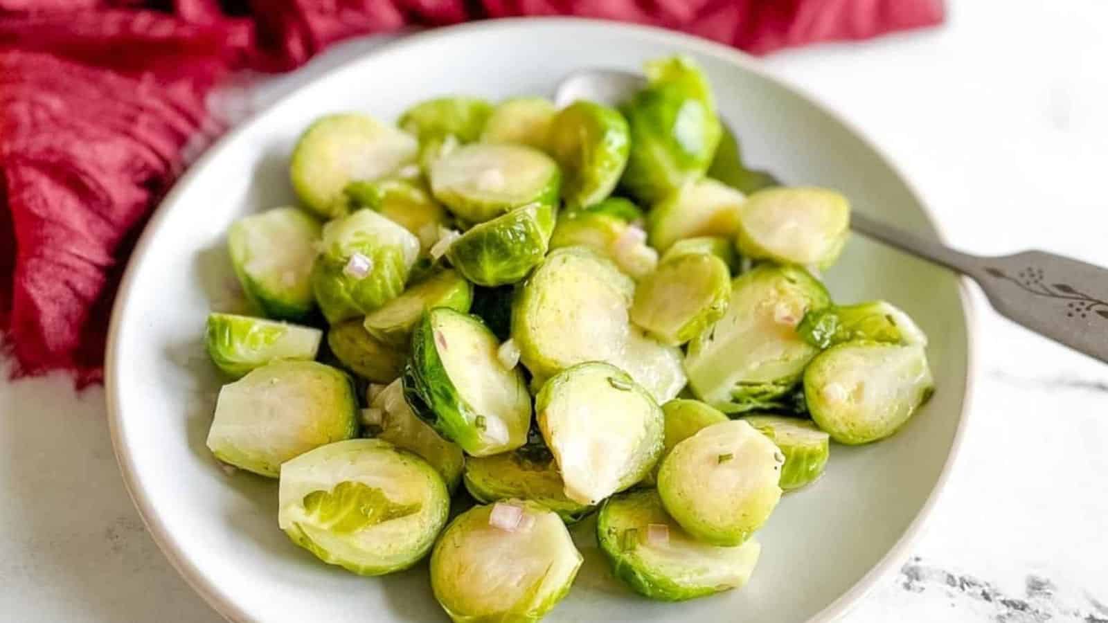 Marinated brussels sprouts are shown on a white plate with a spoon and a dark red linen in the background.