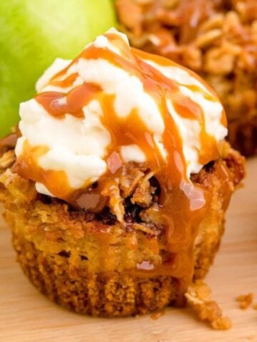 Three Mini Caramel Apple Cheesecakes with Streusel Topping on a wooden board with green apples.