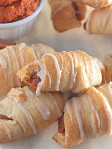 Mini pumpkin crescent rolls with dipping sauce on a plate.