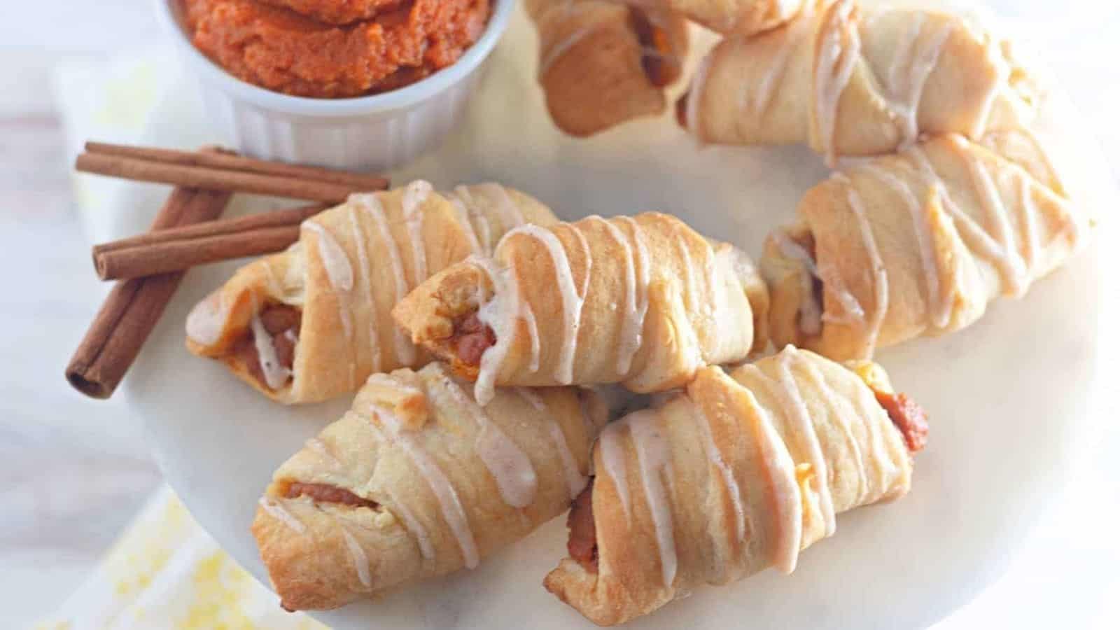 Mini pumpkin crescent rolls with dipping sauce on a plate.