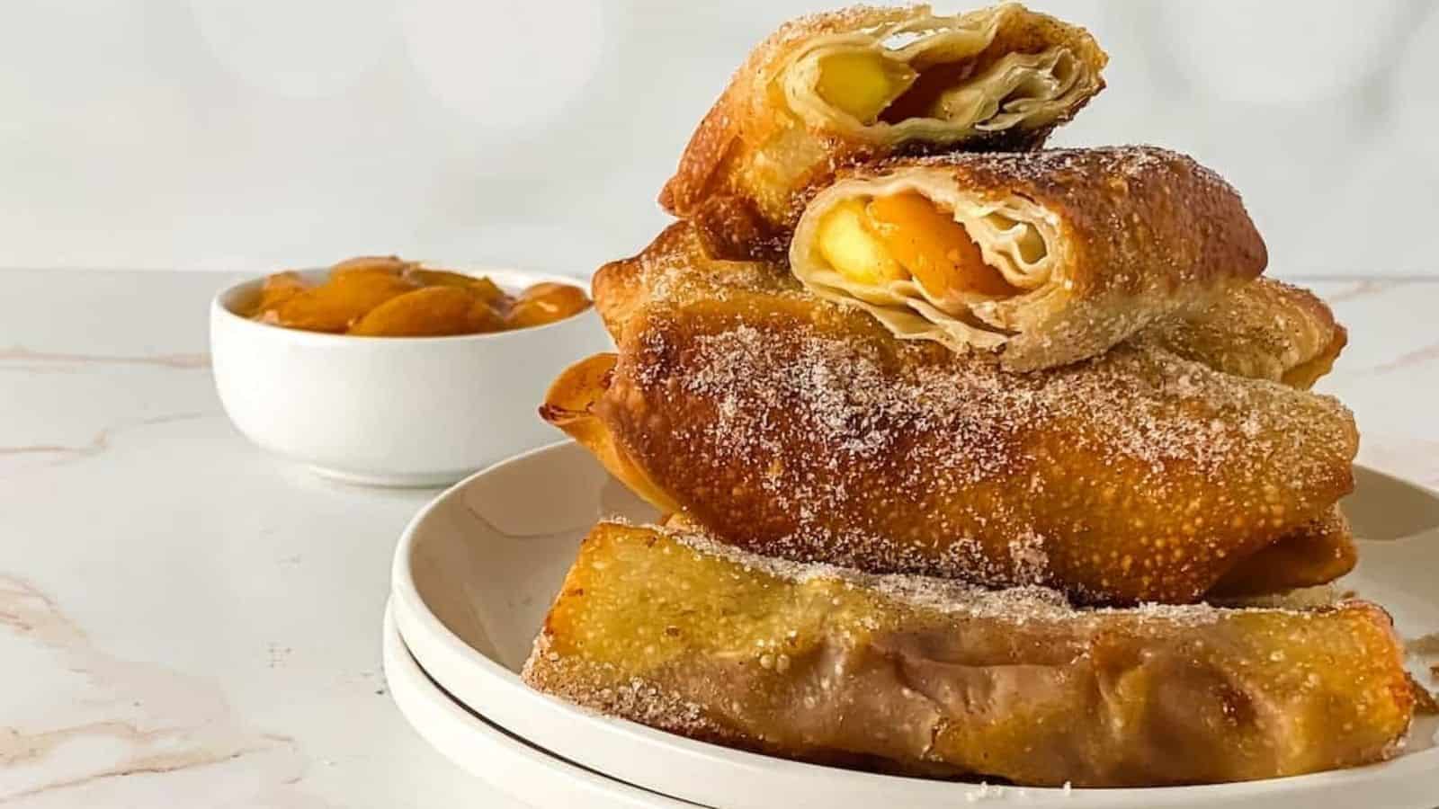 A plate with a stack of peach cobbler egg rolls pastries on it.