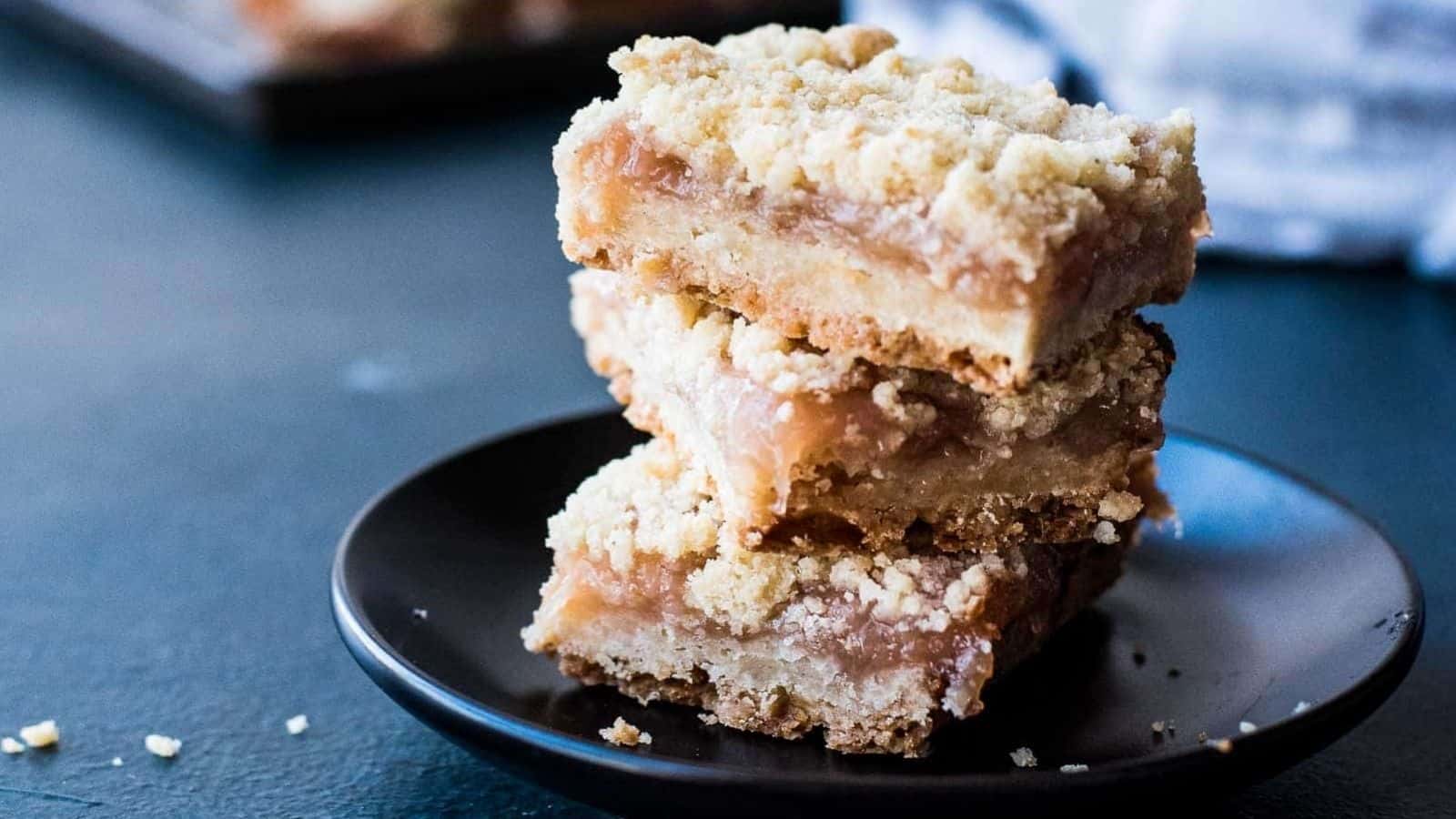 A stack of three peach crumble bars on a black plate.