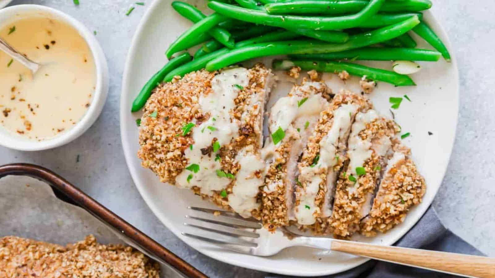 Pecan crusted chicken cut into slices on a plate with honey dijon sauce and green beans.