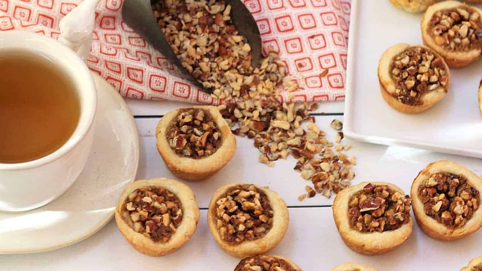 A cup of tea next to a plate of cookies with pecans.