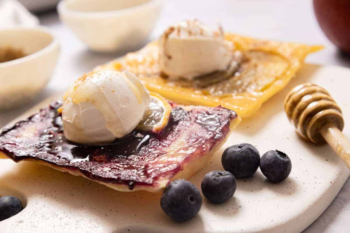 Puff pastry fruit tarts with apples and blueberries on a white board.