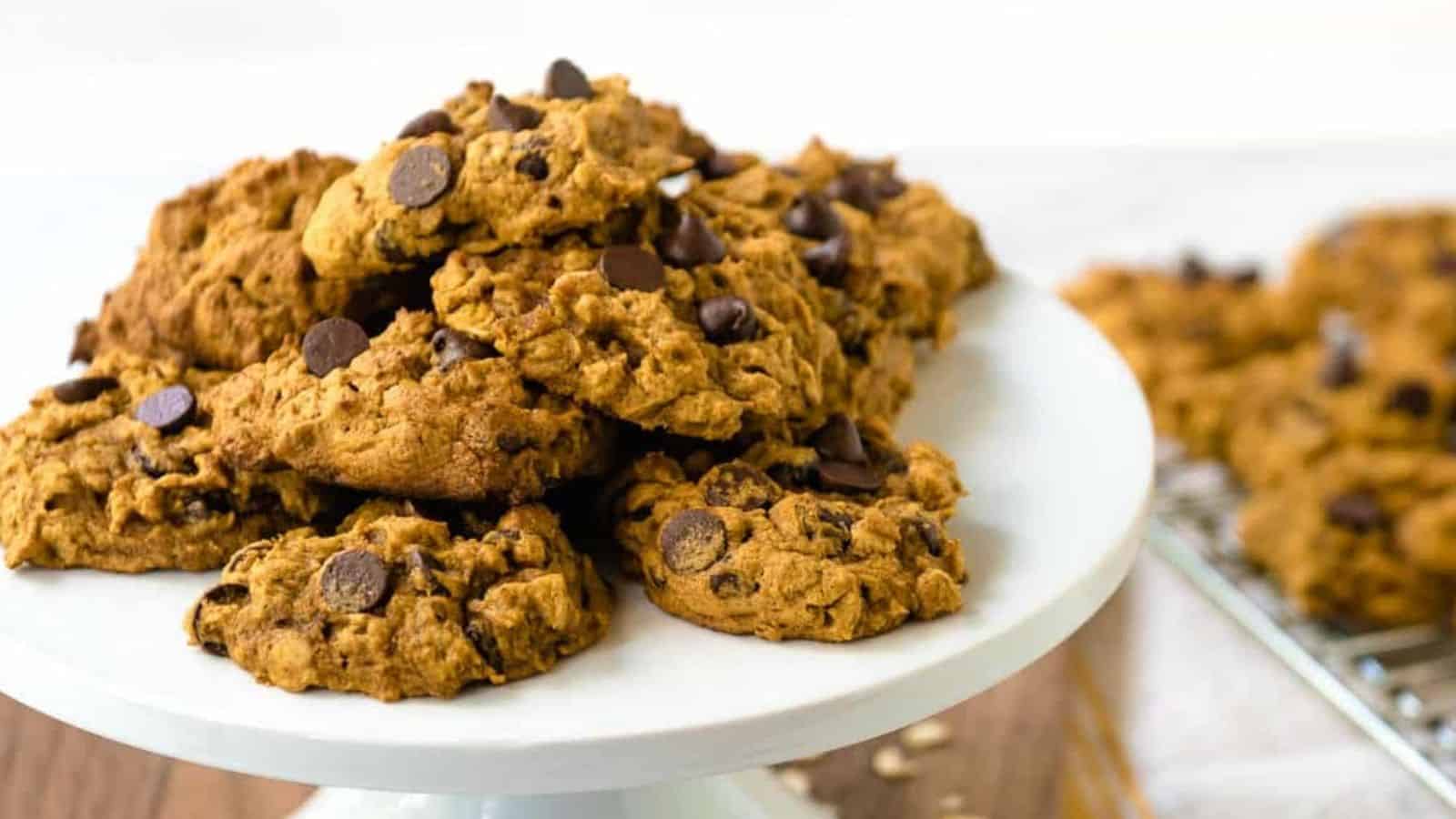 Pile of pumpkin oatmeal chocolate chip cookies with more in the background on a cooling rack.