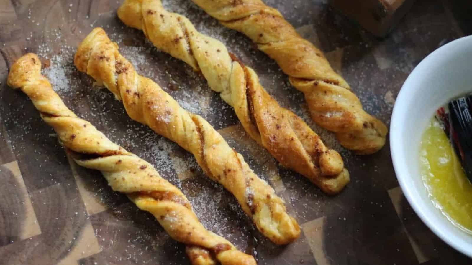 Pumpkin spice churros on a wooden serving board with a bowl of butter off to the right side.