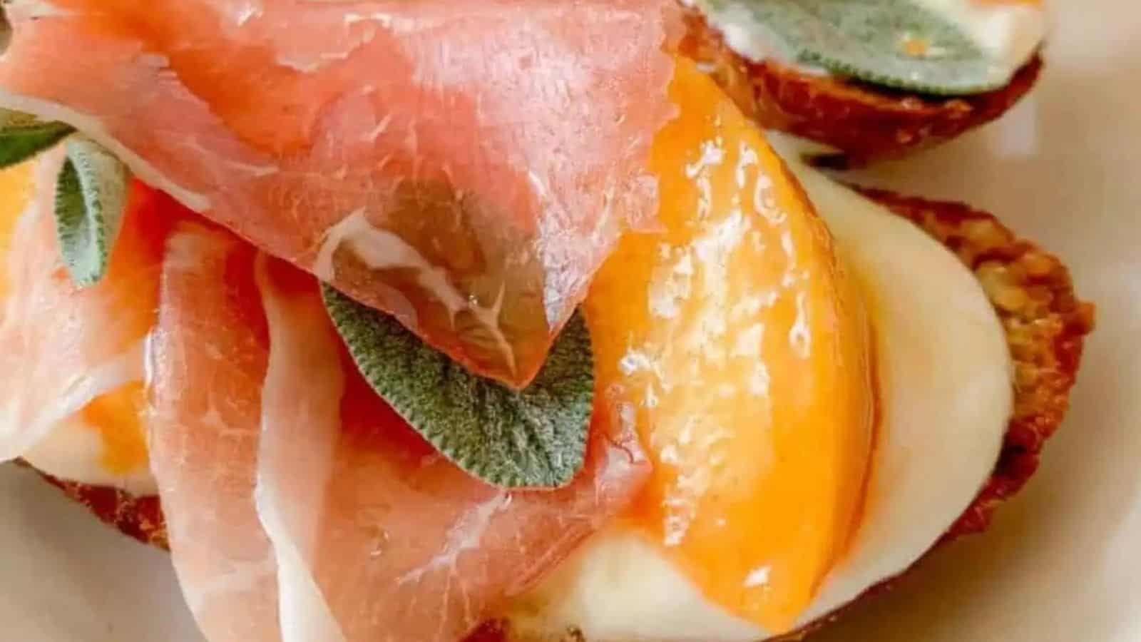 A bite sized piece of crisp bread piled high with prosciutto and peach slices and ricotta cheese.