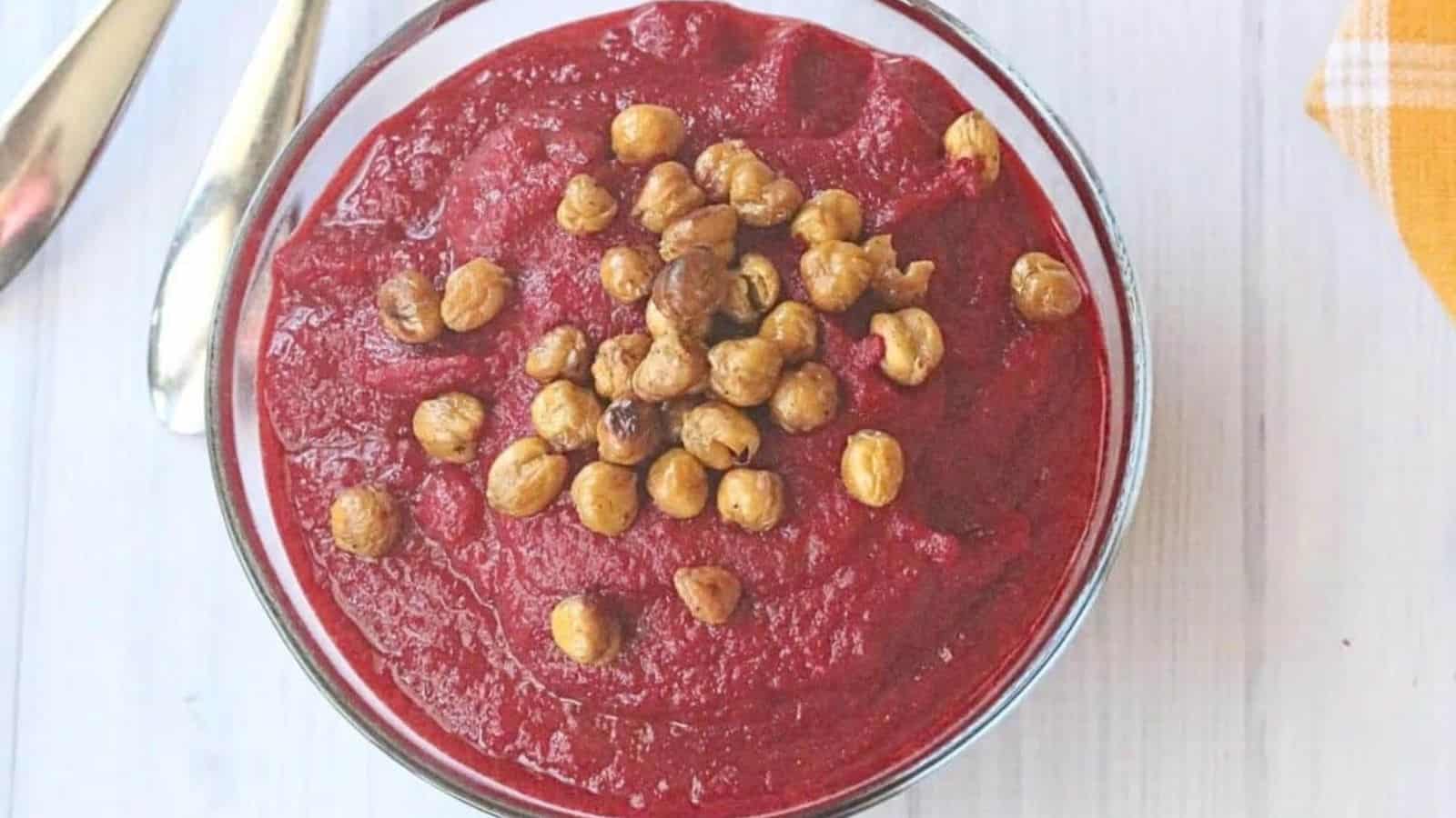 two glass bowls filled with healthy beet soup and topped with chickpeas. Two spoons beside the first bowl and a yellow napkin.