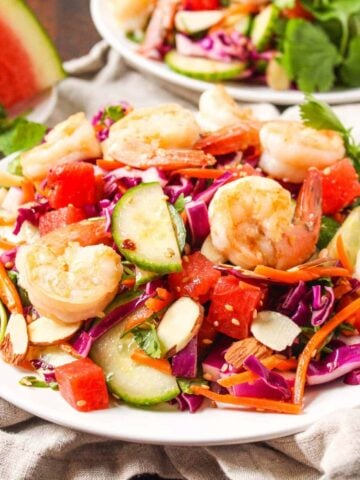 A white plate with shrimp, watermelon, cucumber, shredded cabbage, and grated carrots.