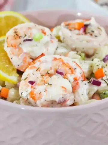 Shrimp macaroni salad in a pink bowl with lemon wedges.