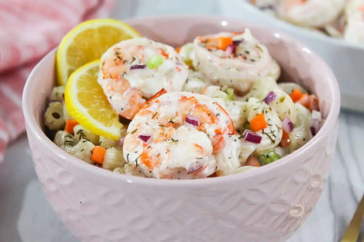 Shrimp macaroni salad in a pink bowl with lemon wedges.