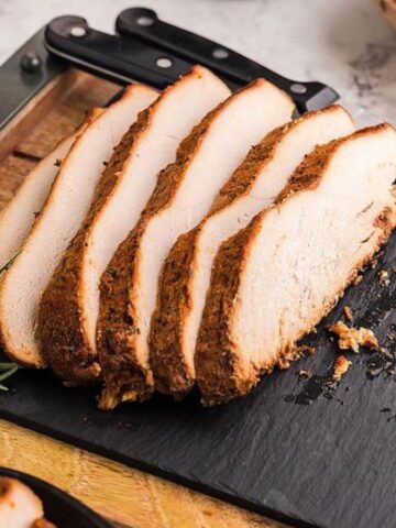 Sliced slow-cooker apple cider brined turkey breast with knife on a cutting board.