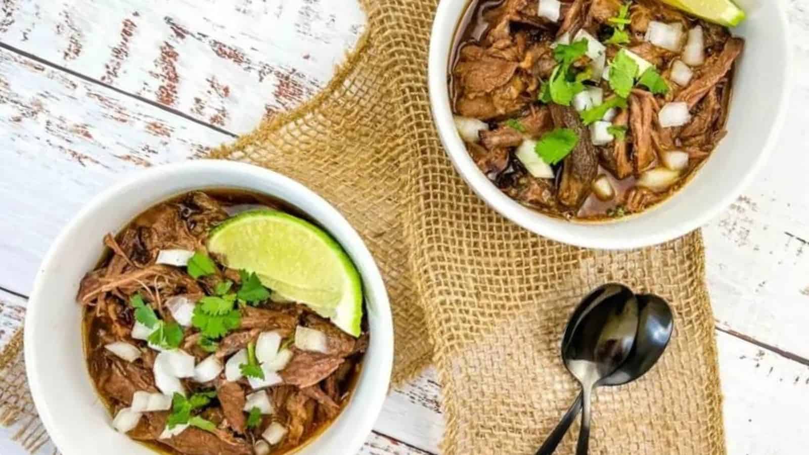 Top view of 2 bowls of slow cooker birria de res on a wooden table.