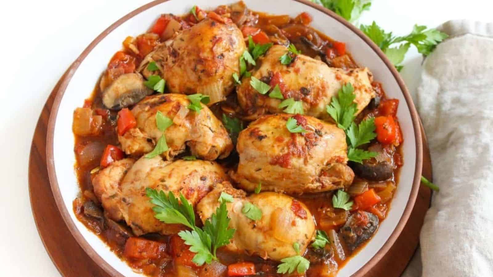 Chicken thighs in tomato sauce on a large white plate.