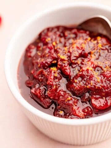 A bowl of Slow Cooker Cranberry Sauce with a spoon and fresh cranberries on the side.