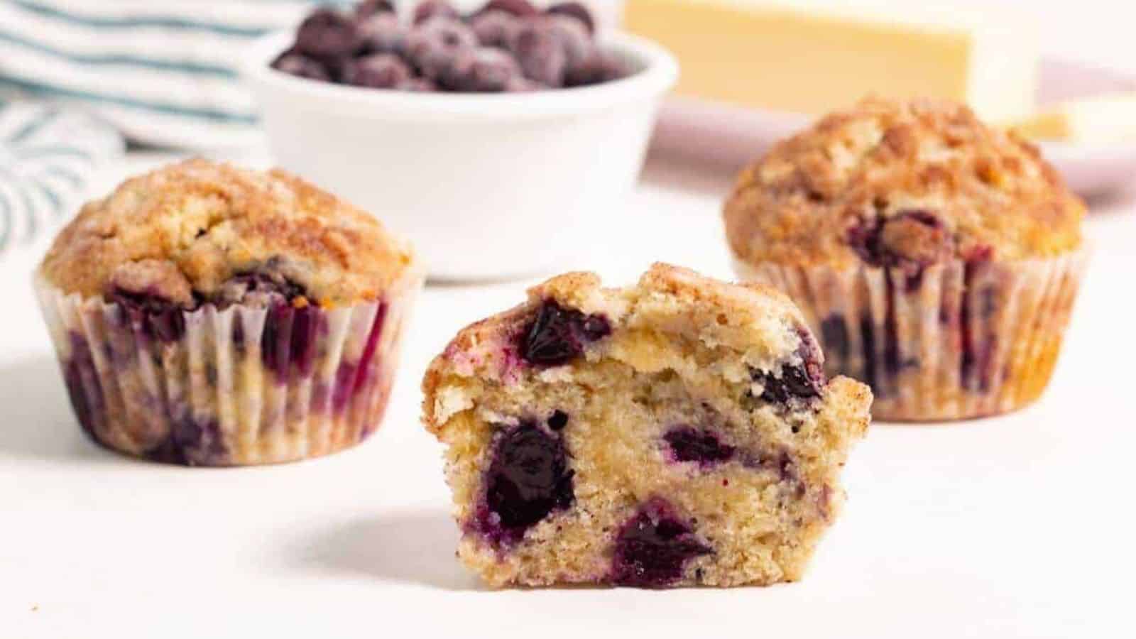 Three blueberry muffins with front one cut in half.