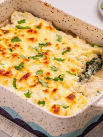 An image of spaghetti squash casserole with a serving missing from the lower right side of the baking dish.