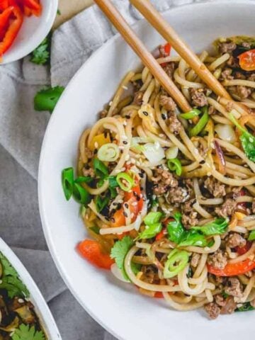 Spicy udon noodle stir fry in a bowl with chopsticks.
