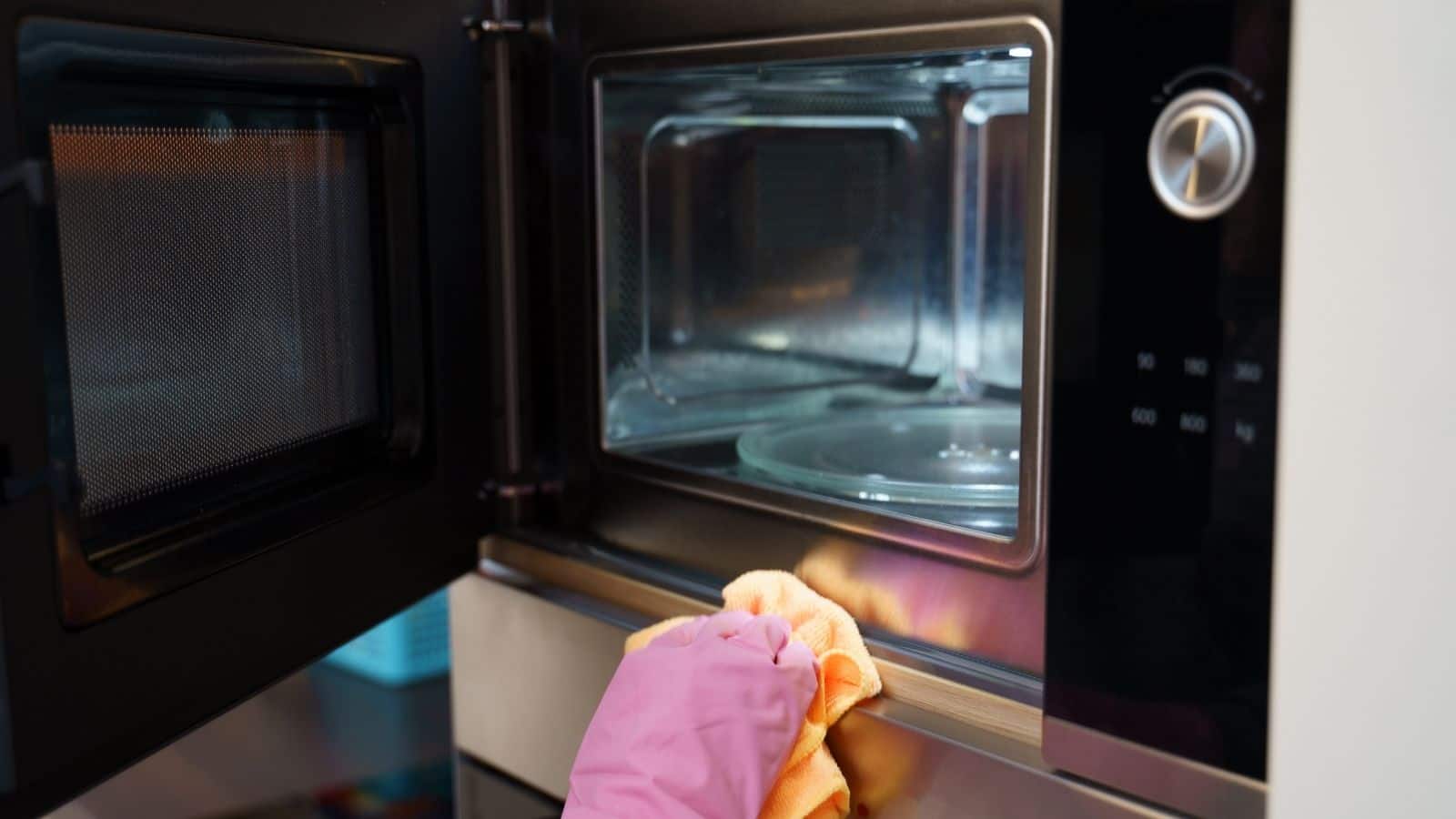 Gloved hand wih an orange towel cleaning microwave.