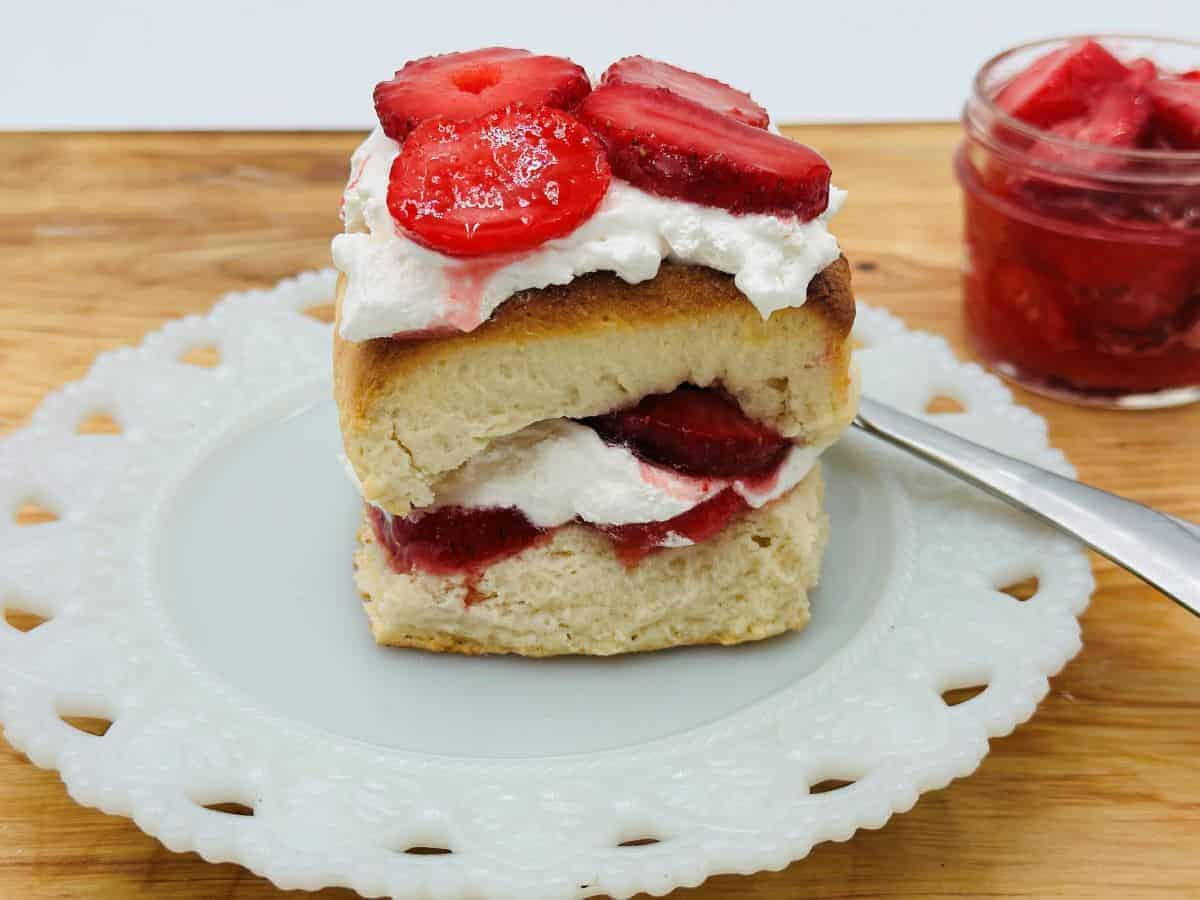 A piece of biscuit with strawberries and whipped cream on a white plate.