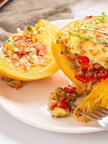 An image of two stuffed spaghetti squashes on a white plate with a fork slicing a part of one of the squashes.