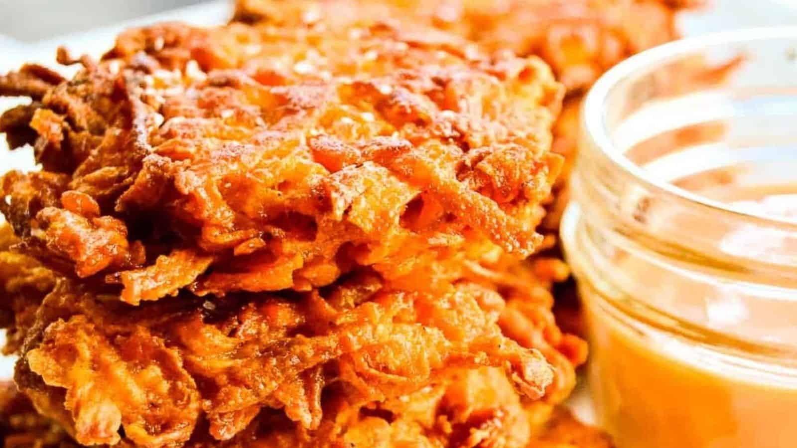 A serving basket of sweet potato fritters next to a bowl of dipping sauce and a single serving on a plate.