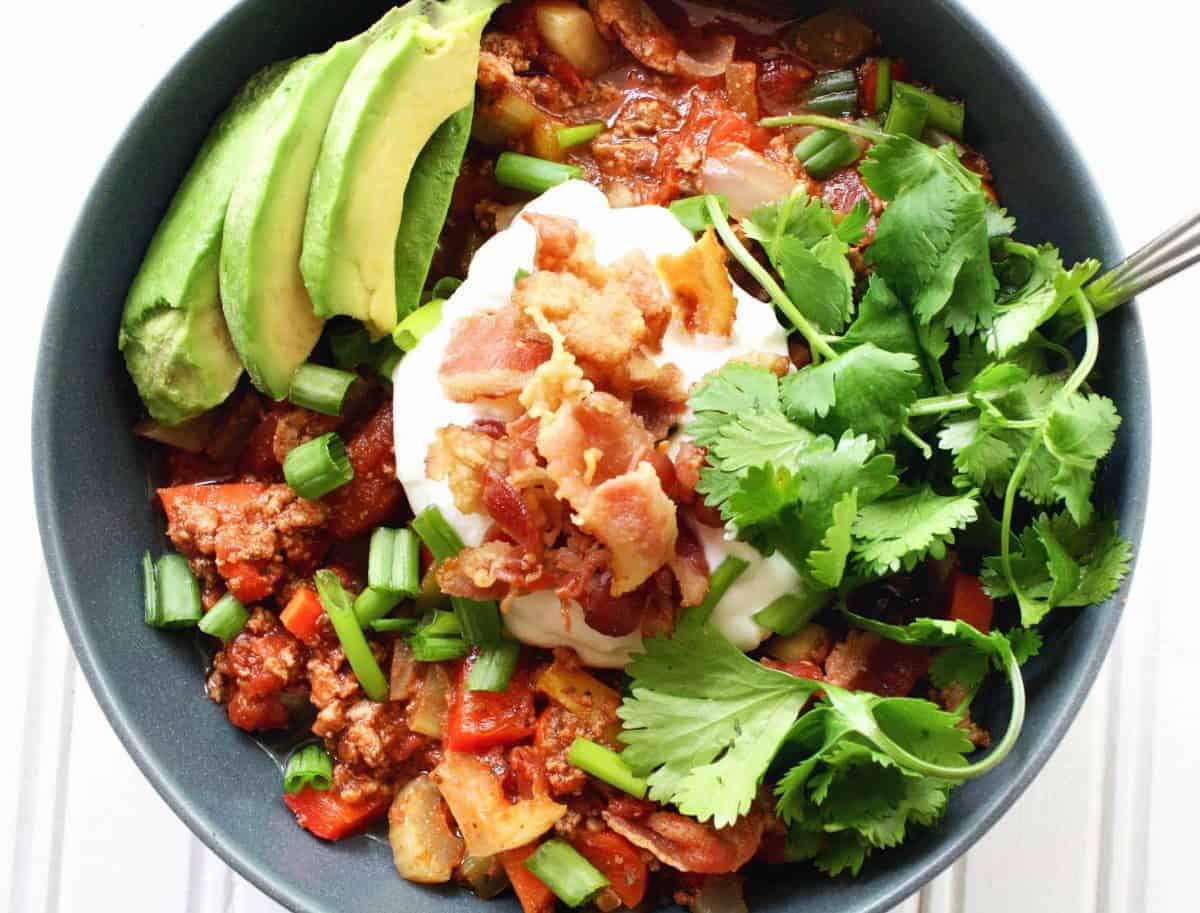 Sweet and spicy bacon and turkey chili garnished with avocado slices, sour cream, and cilantro.