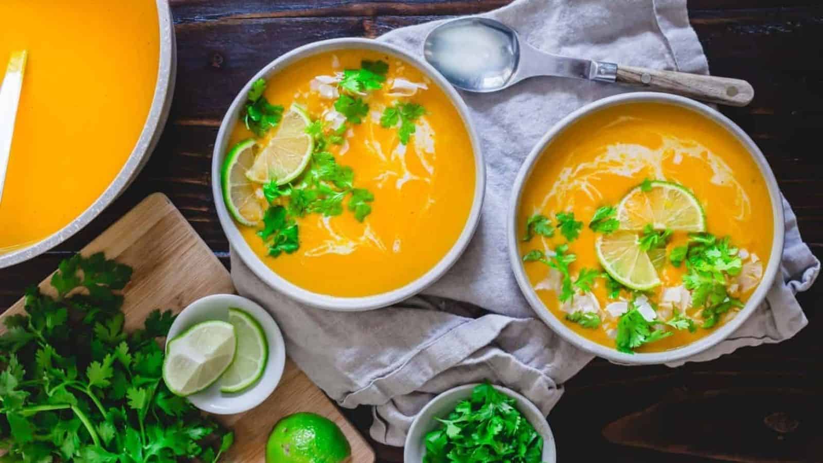 Top view of 2 bowls of thai butternut squash soups topped with greens and sliced lime.