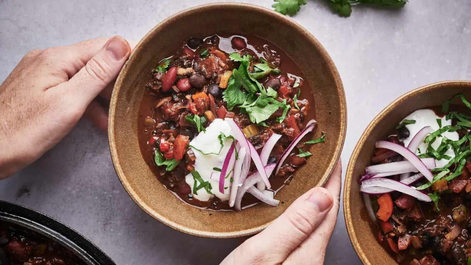 Two bowls of chili with onions and sour cream.