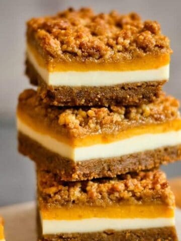 Stack of three pumpkin cheesecake bars on a flat surface.