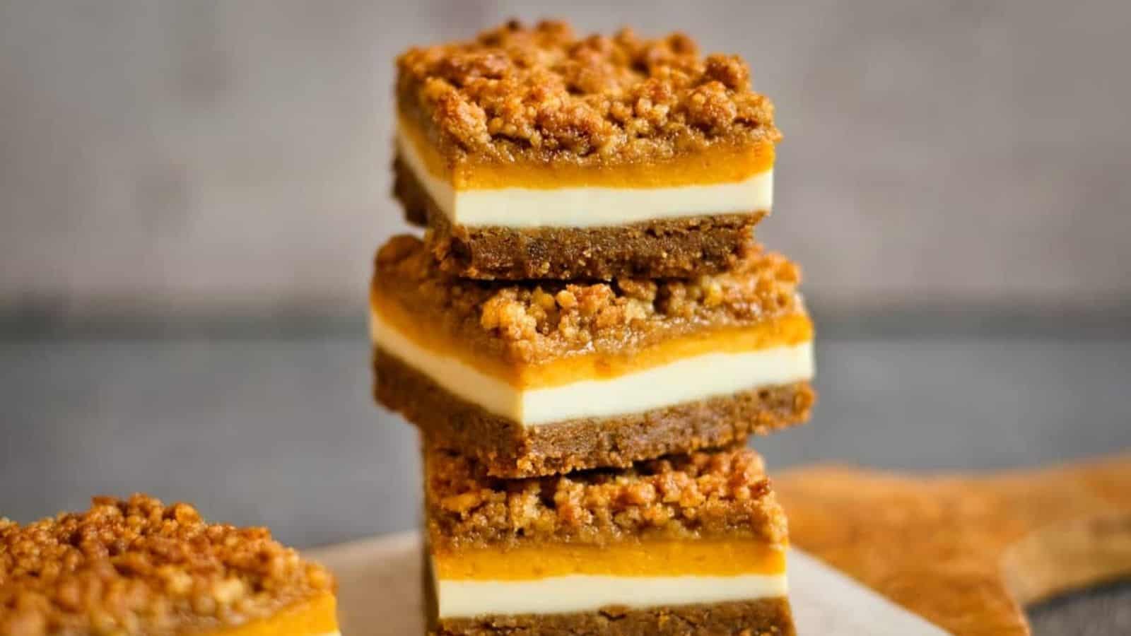 Stack of three pumpkin cheesecake bars on a flat surface.