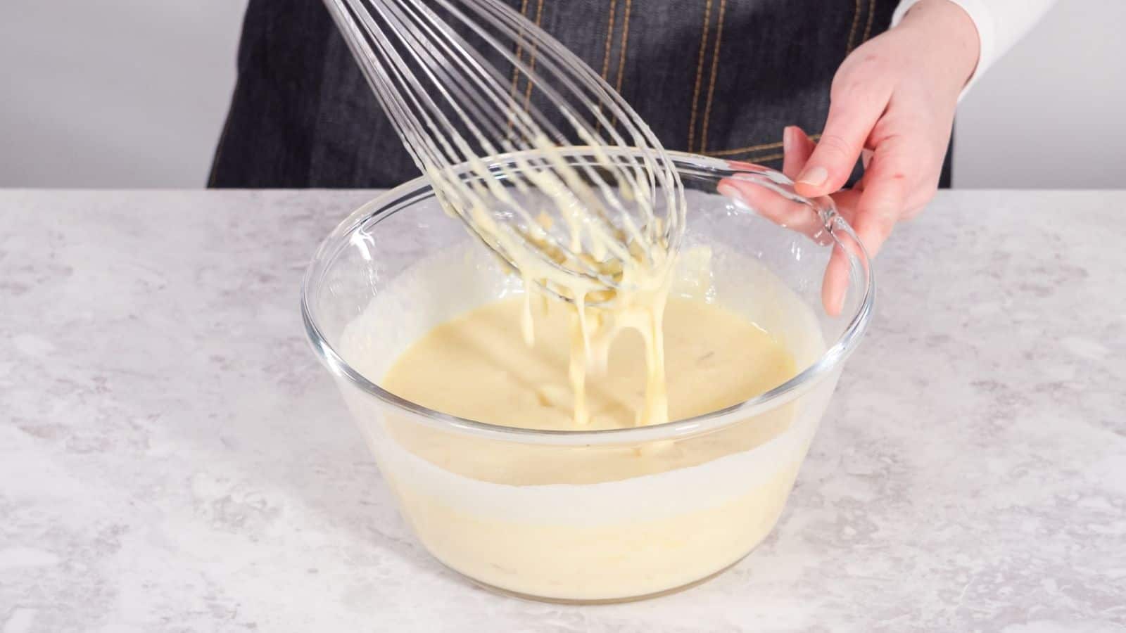 A hand holding a mixer above a batter in a bowl.