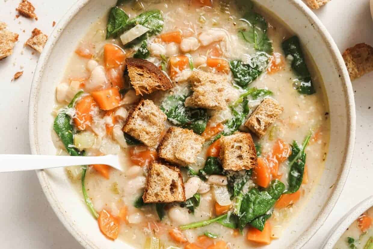 A bowl of white bean soup with carrots and croutons.