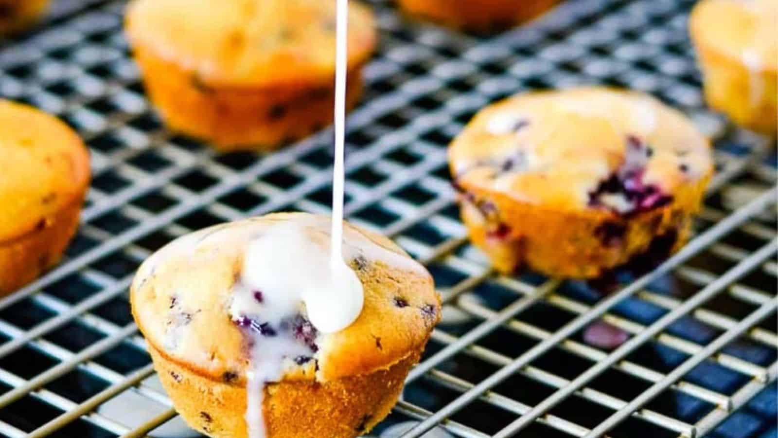 Blackberry muffins drizzled with lemon glaze sitting on a gray cooling rack on a dark background.