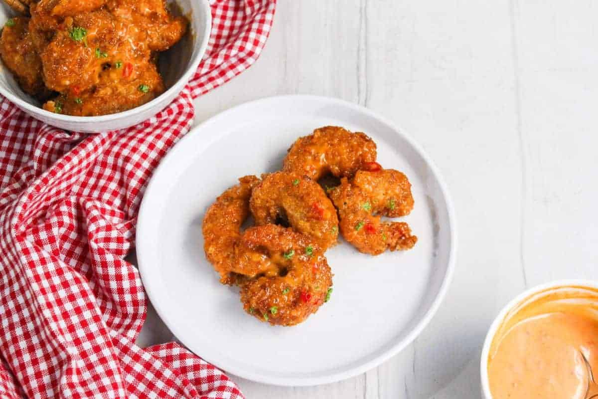 Fried shrimp on a plate next to a bowl of sauce.