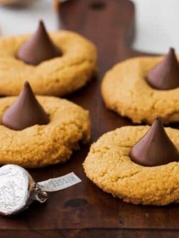 An image of 3 Ingredient Peanut Butter Blossoms on a wooden board with a Hershey’s Kiss.