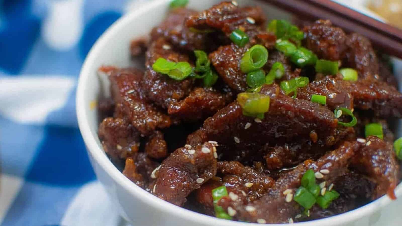 Closeup of crispy beef in a bowl with green onions and sesame seeds.