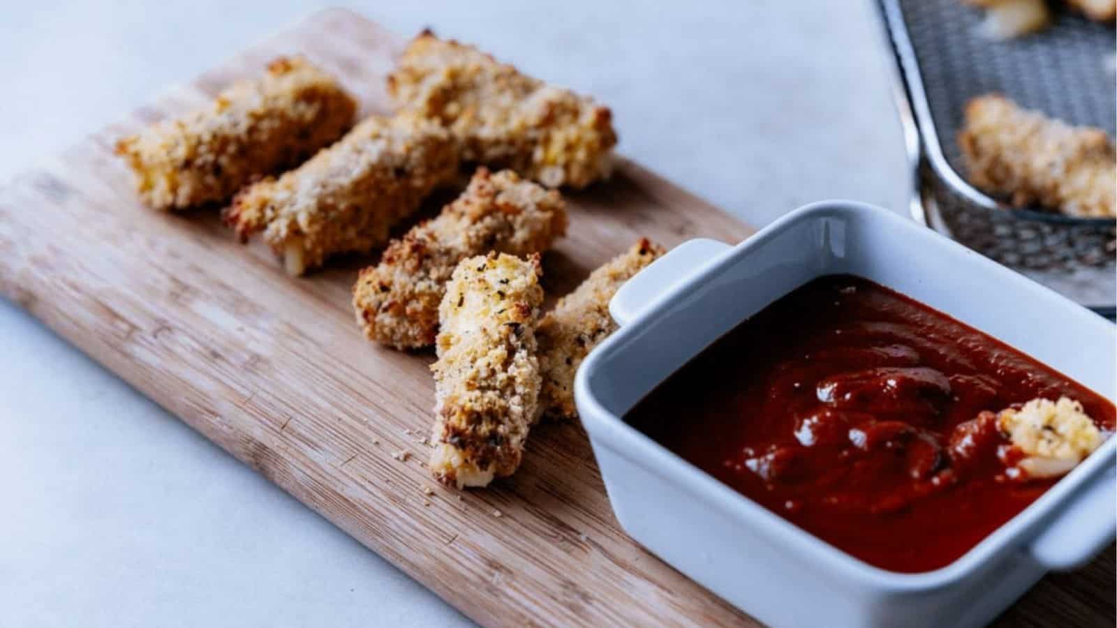 Air fryer mozarella sticks with a dip on a wooden board.