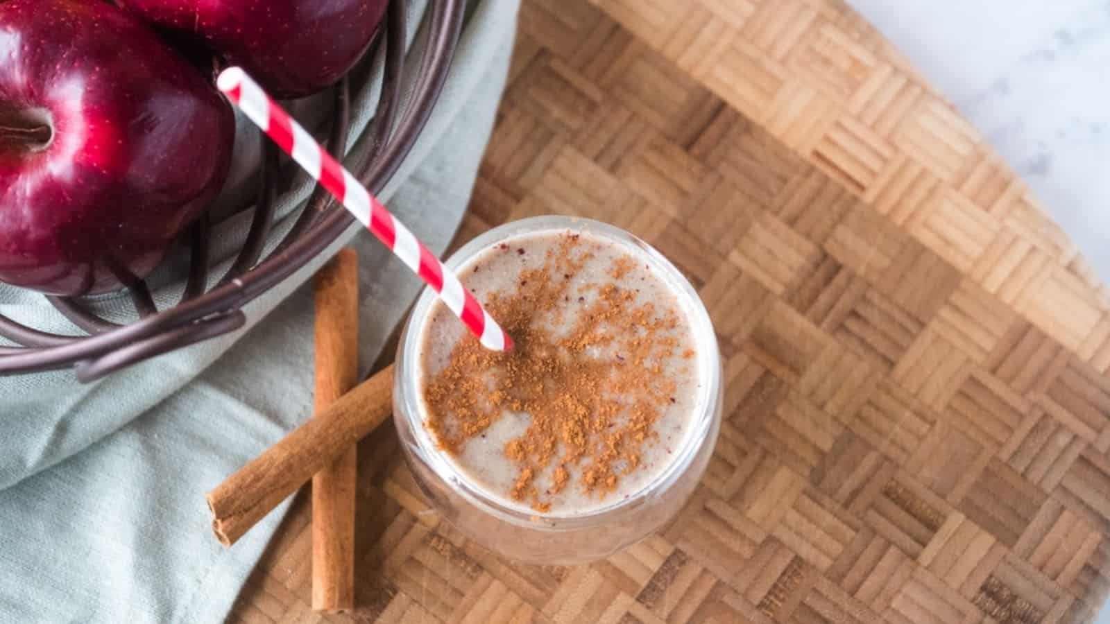 Apple smoothie in a glass with a red polka dot straw on a cutting board.