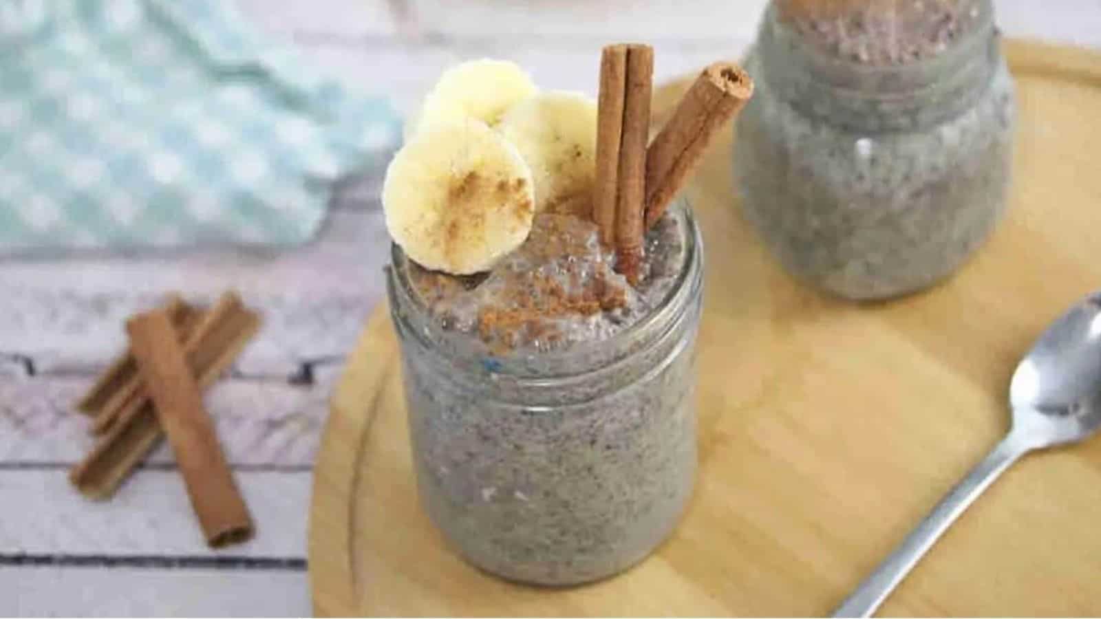 Banana chia pudding in a mason jar with a spoon in it and sliced bananas, and cinnamon on top and the jar on a wooden board.