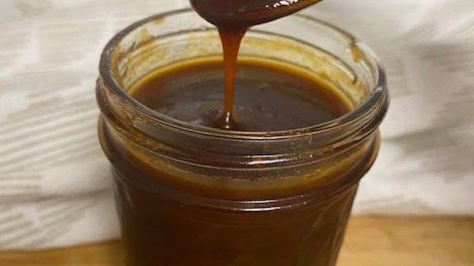 Barbecue sauce in clear jar with spoon dripping above.