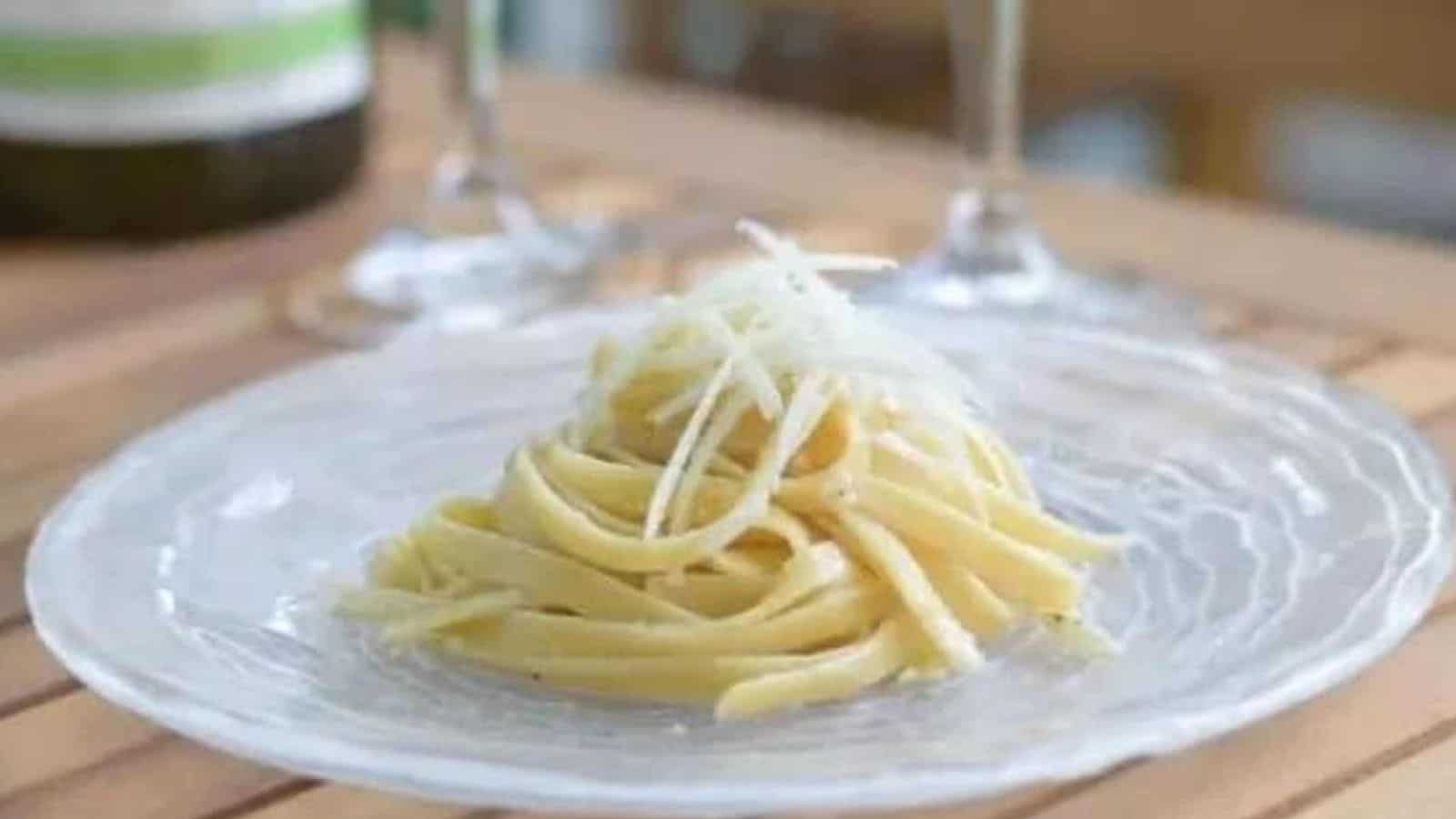 Image shows a plate with cacio e pepe in a neat pile topped with shaved parmesan cheese.