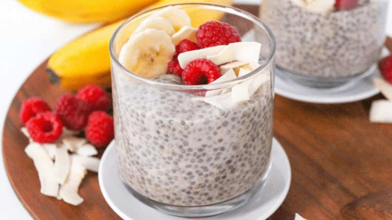 A small glass jar with chia pudding topped with banana slices, coconut flakes, and raspberries.