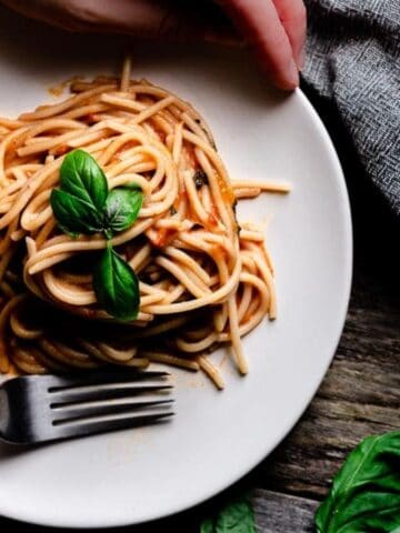 Someone holding a plate of Creamy Tomato Basil Pasta with a fork.
